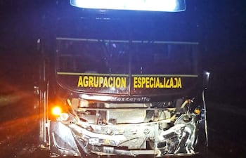 Autobús accidentado de la 'Agrupación Especializada' con daños en la parte delantera, luces encendidas en la carretera oscura.