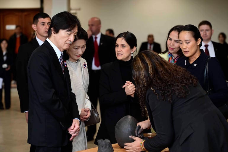 Adriana Ortiz Semidei vestida con atuendo claro observa al Príncipe Imperial Japonés en un evento formal con cerámica en mesa.