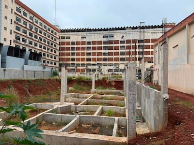 Construcción inconclusa con cimientos de concreto y varillas de hierro, rodeada de vegetación en un entorno urbano.