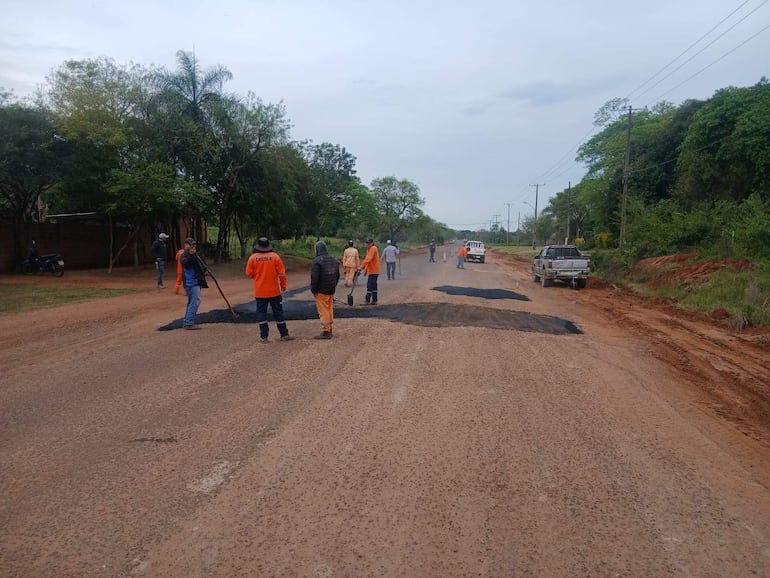 Grupo de trabajadores en camisetas naranjas repara carretera de tierra, con herramientas, bajo un ambiente tranquilo con vegetación.