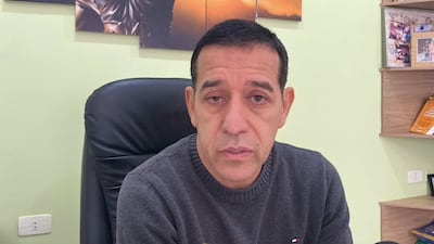 Celso Morales, con suéter gris y expresión seria, sentado en una silla de oficina con fondo verde claro y estantes.