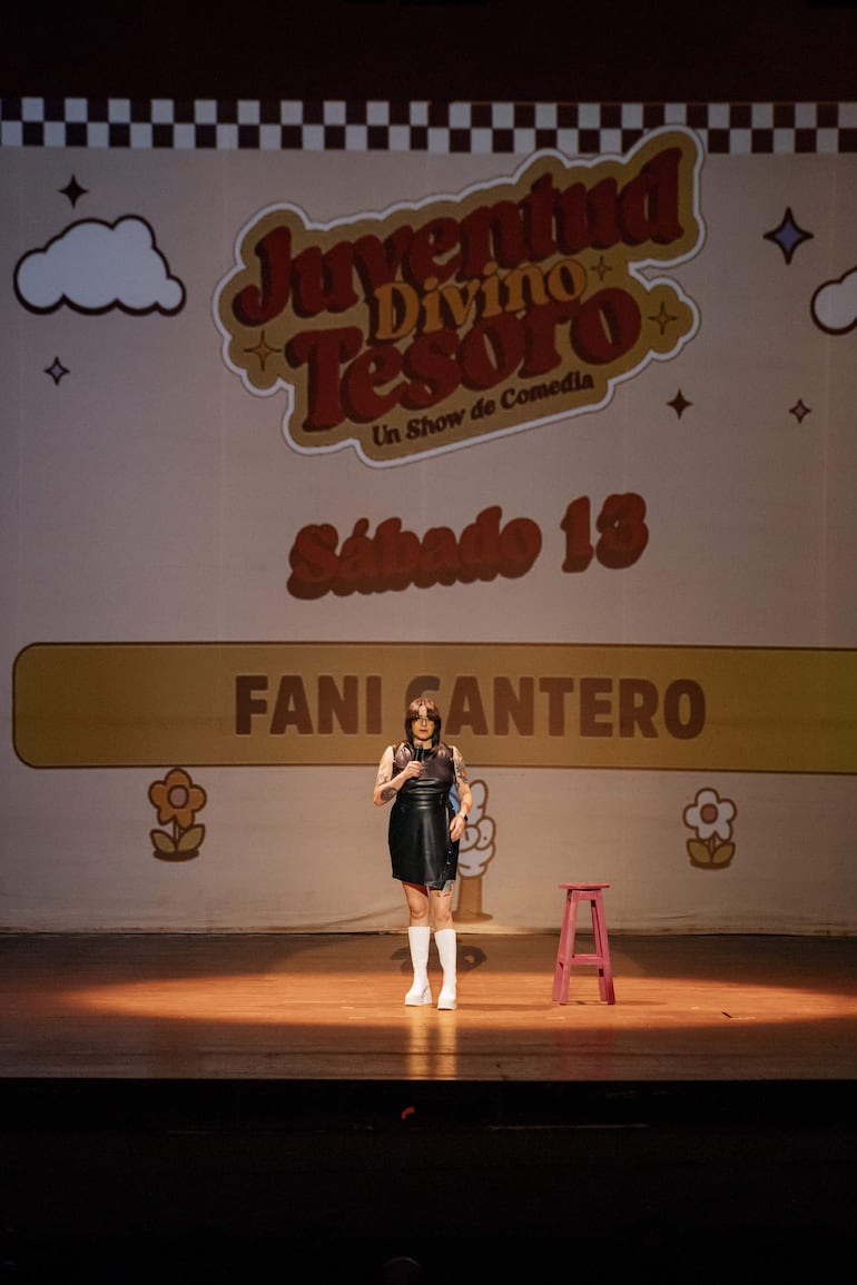 Fani Cantero en vestido negro y tacones blancos, sosteniendo un micrófono en el escenario con fondo colorido.
