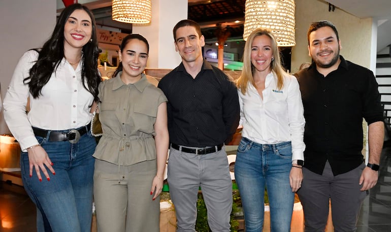 Cinco personas sonríen y posan, vistiendo ropa casual en un entorno iluminado y moderno.