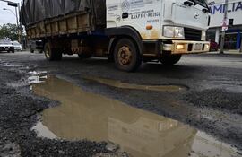 Camión de carga en Avenida Artigas, rodeado de baches y charcos de agua en una calle deteriorada.