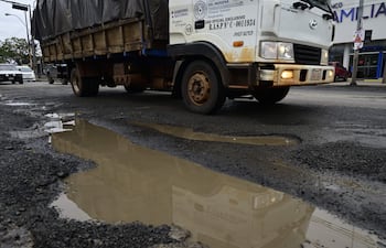 Camión de carga en Avenida Artigas, rodeado de baches y charcos de agua en una calle deteriorada.