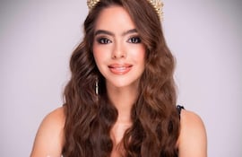 Mujer con cabello largo y ondulado, sonriendo, lleva tiara dorada y vestido negro en fondo neutro.