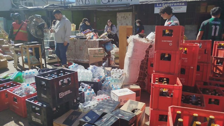 Hombres y mujeres en el mercado de Itauguá, rodeados de pallets y cajas de productos, bajo un día soleado.