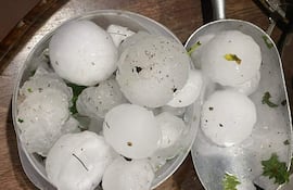 Bandeja y recipiente con bolas de granizo, manchas de tierra visibles, sobre superficie de madera.