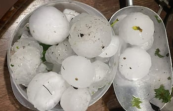 Bandeja y recipiente con bolas de granizo, manchas de tierra visibles, sobre superficie de madera.