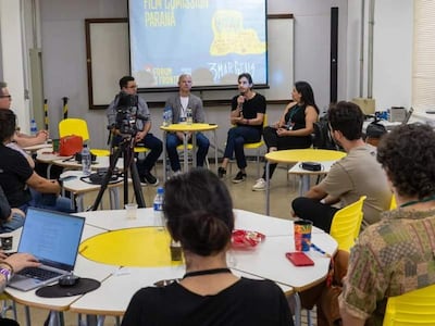Panel de discusión con cuatro personas, incluidas un hombre hablando con micrófono y una mujer con cabello largo y vestido negro.
