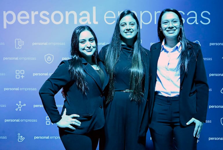 Tres mujeres vestidas de negro sonríen en un salón de eventos, con un fondo que sugiere un evento empresarial.