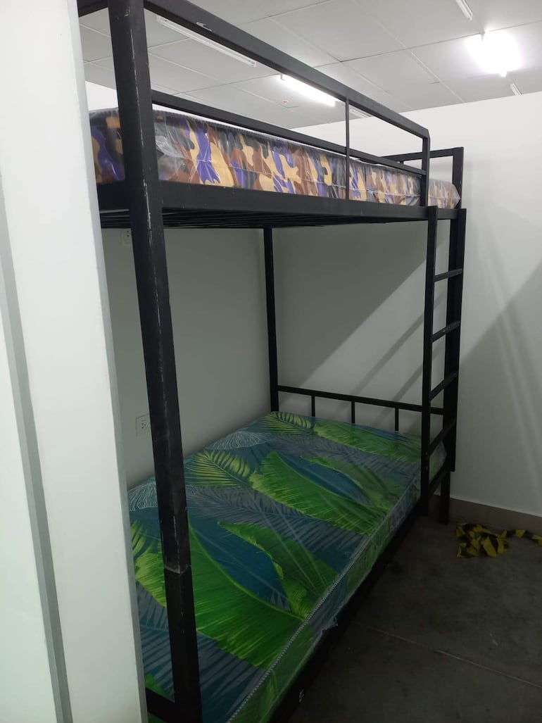 Litera de metal en ambiente sencillo con colchones de camuflaje y verde, preparado para recibir a familiares.