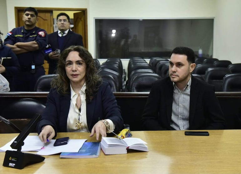 Alba Zaracho habla gesticulando, mientras Hernán Rivas escucha con atención; ambos en un entorno formal y bien iluminado.