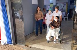 Una mujer en silla de ruedas es asistida por un profesional, mientras otros tres individuos con mascarillas conversan en un ambiente con luz natural.
