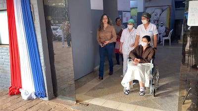 Una mujer en silla de ruedas es asistida por un profesional, mientras otros tres individuos con mascarillas conversan en un ambiente con luz natural.