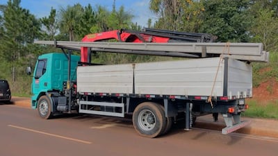 Camión verde claro con grúa roja transportando estructuras de hormigón en un entorno tranquilo con vegetación.