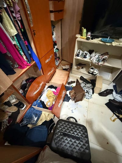 Habitación desordenada con armario de madera, maleta negra y ropa esparcida por el suelo.