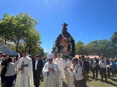 Procesión con un altar portátil de la Virgen María, rodeado de sacerdotes y fieles en un día soleado.
