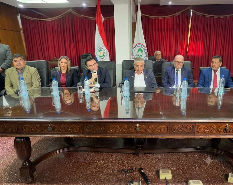 Seis personas participan de una conferencia de prensa. El asesor Carlos Pereira, de traje oscuro, hace uso de la palabra.