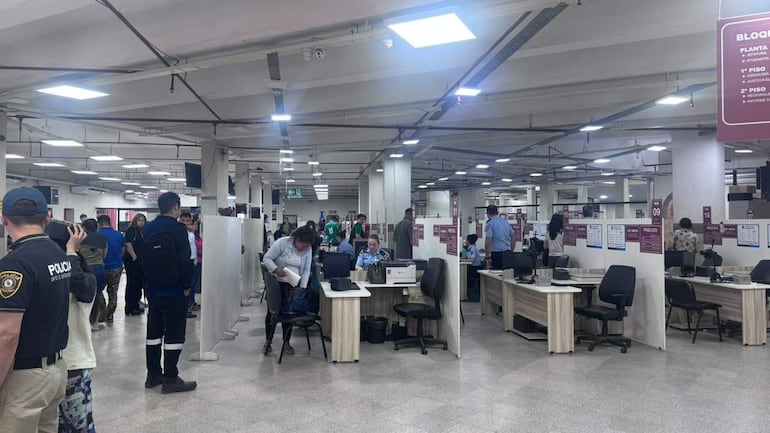 Hombres y mujeres en un espacio administrativo, algunos con documentos, conversando con un policía en uniforme.