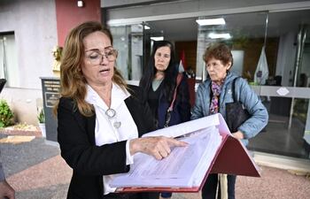 Mujer de cabello castaño claro y chaqueta negra expone, rodeada de tres personas atentas en un ambiente oficial.