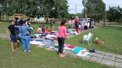 Grupo de personas, incluidos adultos y niños, seleccionan ropa en césped, con un perro sentado al lado derecho.
