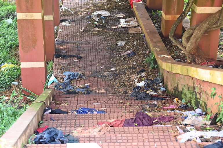 Área descuidada del Parque Verde, con pavimento cubierto de desechos como ropa y plásticos, sin presencia de personas.
