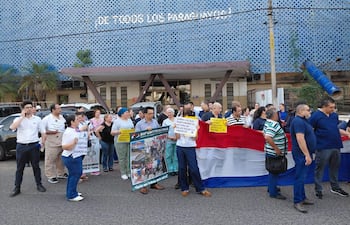 Grupo de personas con uniformes médicos sosteniendo carteles y una bandera de Paraguay, manifestándose junto a un edificio público.