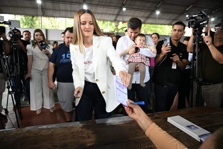 Soledad Núñez con chaqueta blanca y camiseta 'ACTÚO' entrega un documento, mientras Bruno Defelippe la observa con tranquilidad.