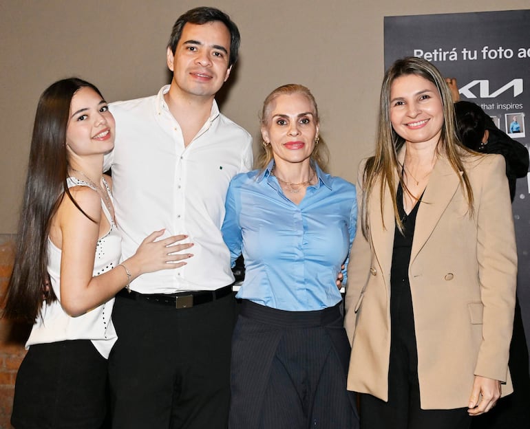 Cuatro personas sonríen juntas en ambiente decorado con tonalidades neutras, un hombre en camisa blanca y dos mujeres en blusas coloridas.