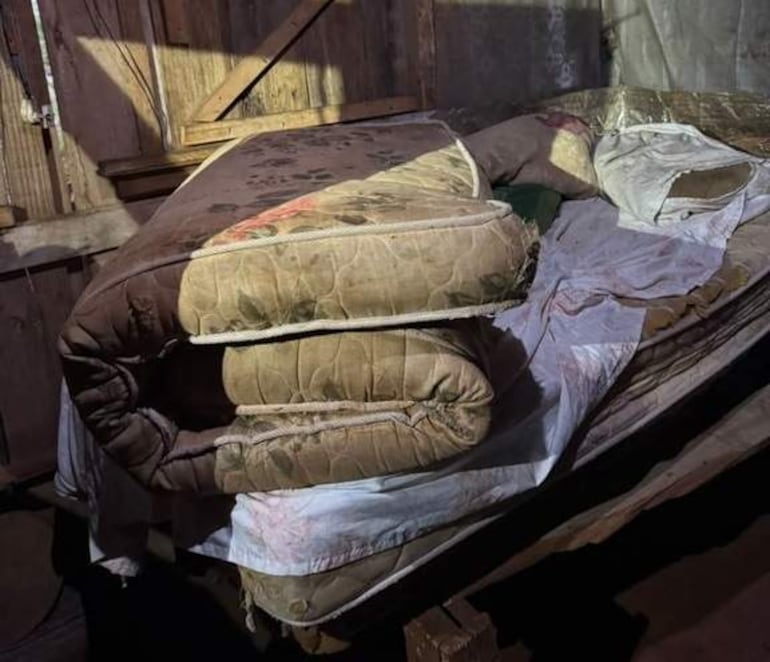 Habitación descuidada con cama y colchones apilados, mostrando signos de abandono y falta de higiene.