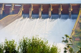 Represa Itaipú con compuertas abiertas liberando agua a gran caudal en un entorno natural con vegetación.