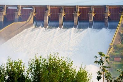 Represa Itaipú con compuertas abiertas liberando agua a gran caudal en un entorno natural con vegetación.