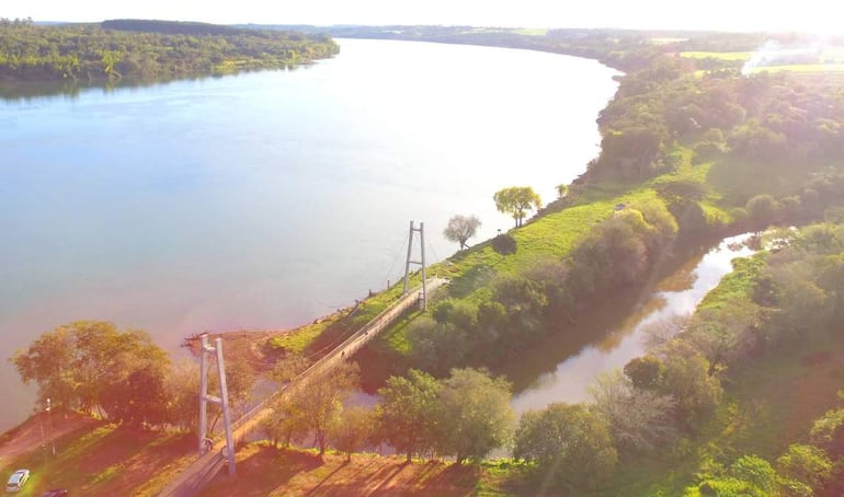 Puente colgante cruzando un río rodeado de vegetación en un ambiente natural tranquilo.