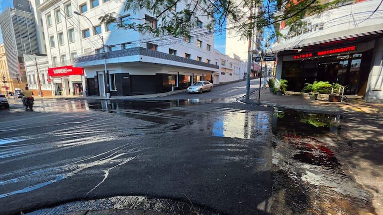 Calle del microcentro de Asunción con pavimento mojado, vehículos y comercios destacados como SUDAMERIS y OLIDERS.