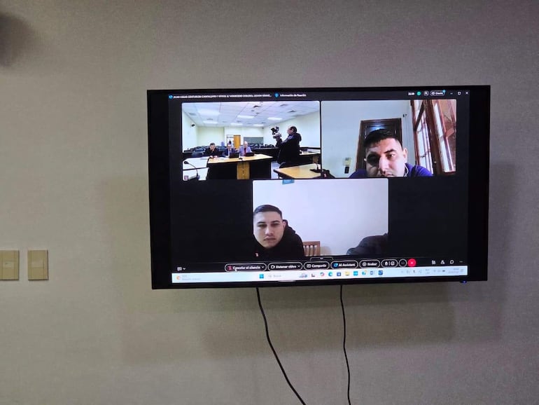 Videoconferencia con cuatro personas, una de pie hablando y tres sentadas escuchando, en un ambiente iluminado artificialmente.