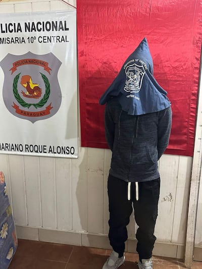 Joven de espaldas en comisaría, con sudadera azul y pantalones oscuros, frente a cartel de la Policía Nacional.