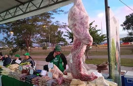 Hombre con gorro verde y delantal sostiene un teléfono, rodeado de productos alimenticios en un ambiente festivo.