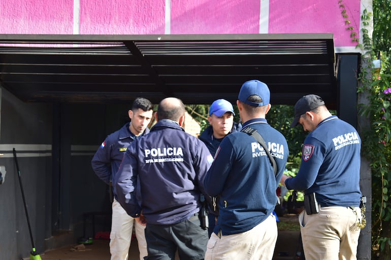Cuatro policías conversan, uno con chaqueta blanca y otro con gorra azul, en un entorno exterior de paredes rosa.