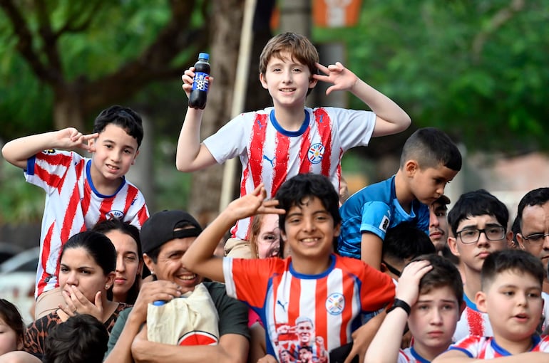 Niños con camisetas de la APF sonríen y juegan, en un ambiente festivo al aire libre con árboles de fondo.