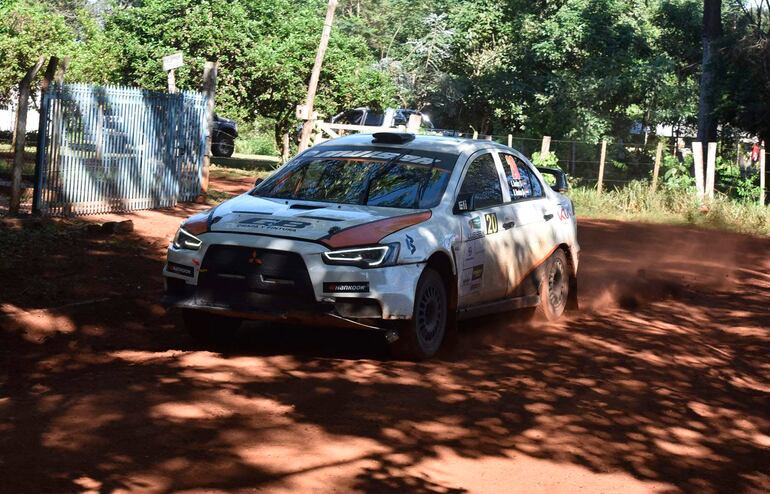 Mitsubishi en movimiento levantando polvo en una ruta de tierra, surrounded by dense vegetation.