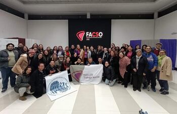 Grupo de 50 personas en la Facso-UNA, todos sonrientes y sosteniendo cartelones sobre trabajo social, en un ambiente festivo.