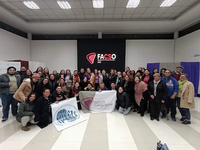Grupo de 50 personas en la Facso-UNA, todos sonrientes y sosteniendo cartelones sobre trabajo social, en un ambiente festivo.