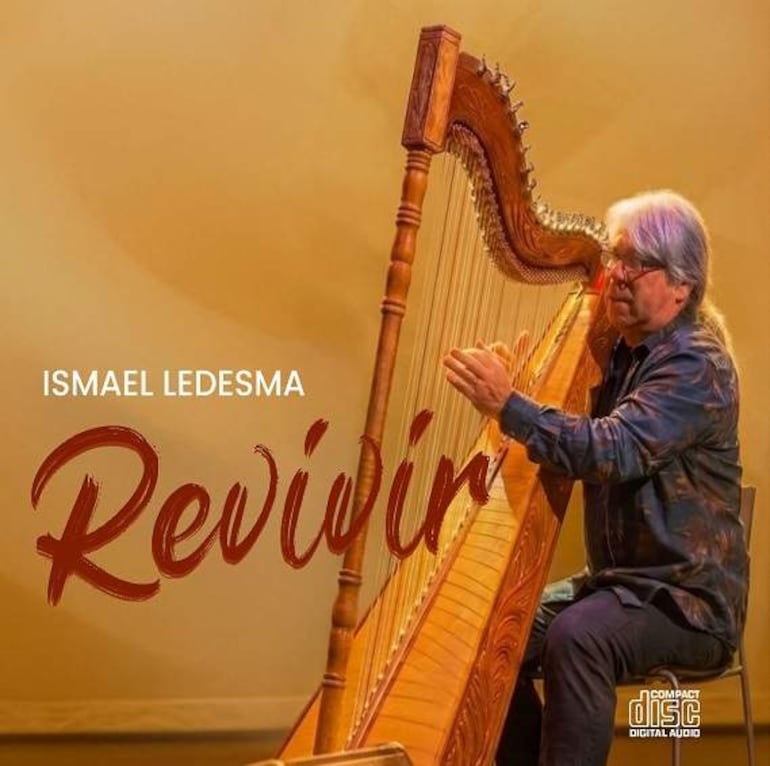 Ismael Ledesma, con cabello canoso y camisa oscura, toca el arpa, concentrado en su interpretación en un escenario iluminado.