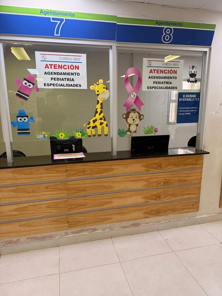 Área de recepción con ventanillas 7 y 8 para agendamiento de pediatría, decoraciones infantiles y carteles informativos.