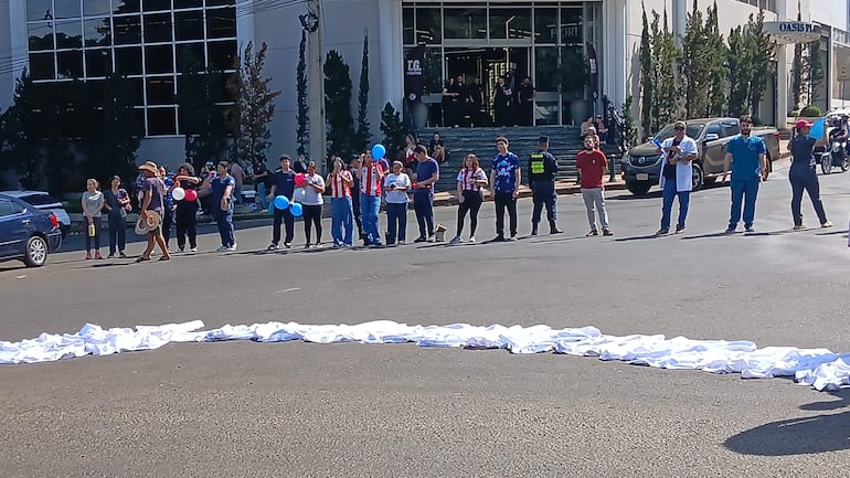 Grupo de 15 personas con camisetas rojas y blancas, sosteniendo globos en un ambiente festivo junto a la carretera.