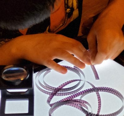Niño inclinado sobre mesa iluminada manipulando cinta de película, con rollos apilados a su alrededor.