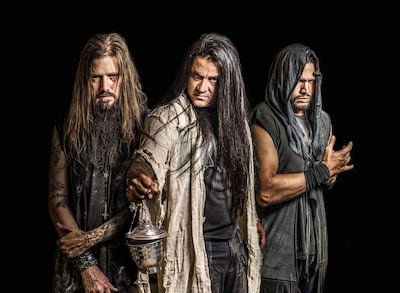 Tres hombres de cabello largo y barba en un fondo oscuro, el del centro sostiene un objeto metálico, mientras los otros lo miran atentos.