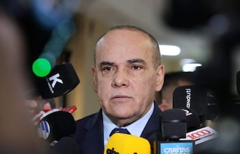 Basilio Núñez en traje oscuro y corbata, rodeado de periodistas con micrófonos, en un ambiente formal de prensa.