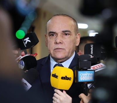 Basilio Núñez en traje oscuro y corbata, rodeado de periodistas con micrófonos, en un ambiente formal de prensa.